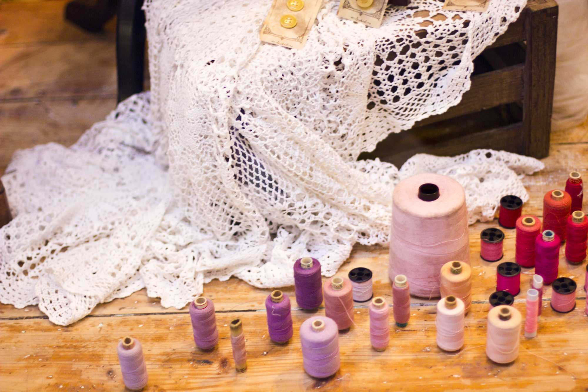 Colorful spools of thread in pink and purple shades arranged on a wooden table next to white crocheted lace