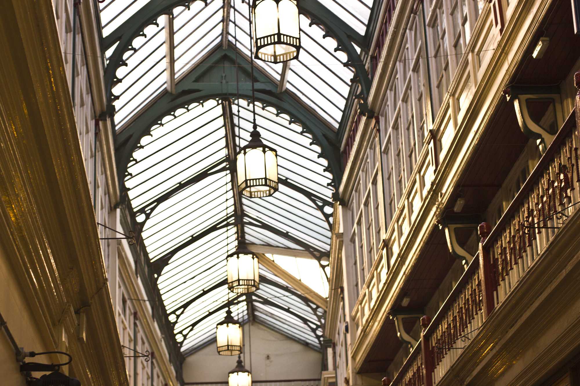 An ornate glass-paneled arched ceiling lit by hanging lantern lights, warm gold against deep shadows